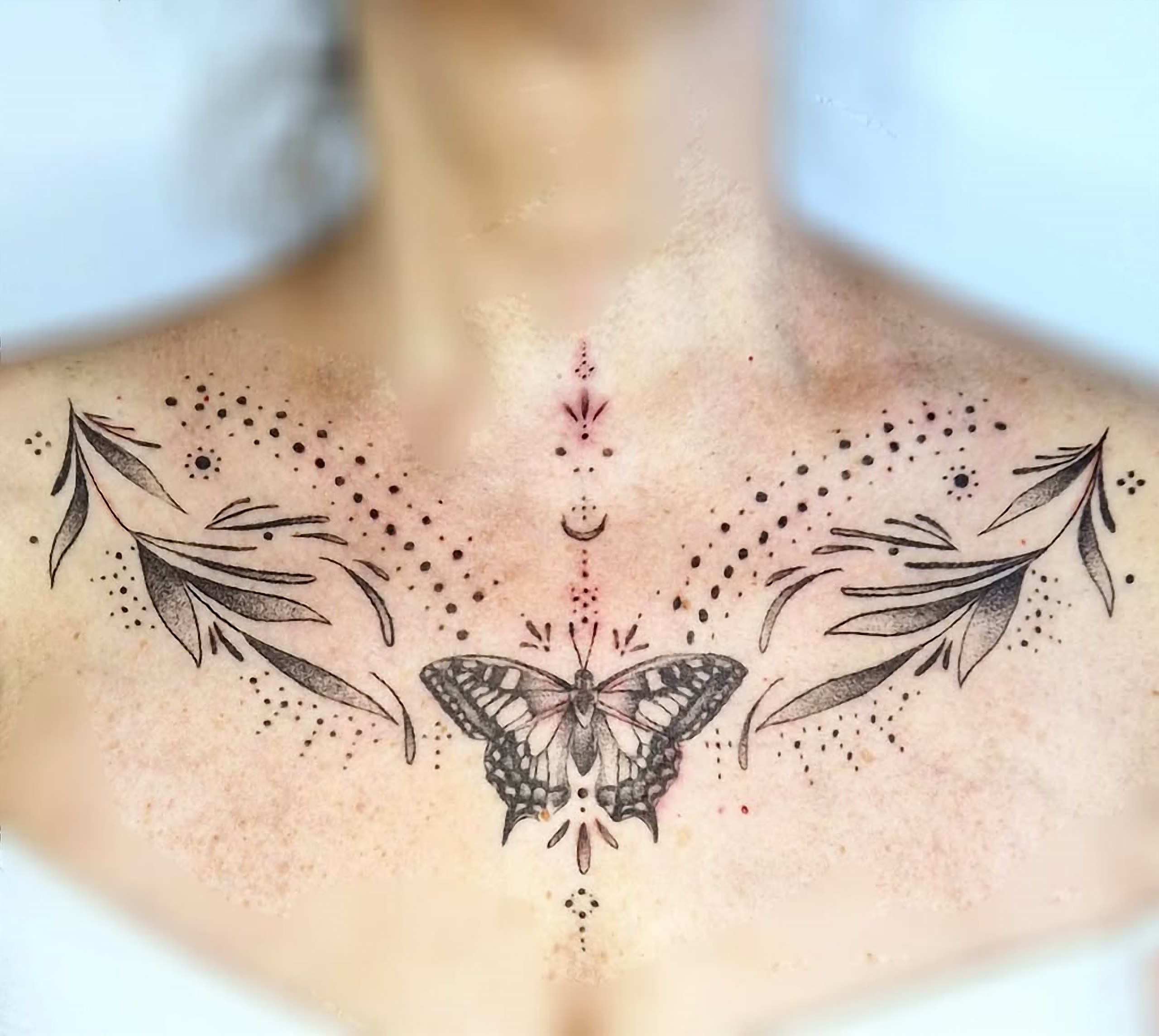Tatouage papillon et feuillages sur le sternum, en noir et gris fine-line.